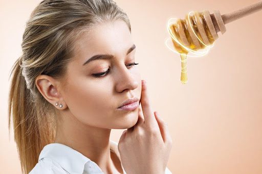 A young woman with honey-blonde hair poses next to an enlarged honey spoon.