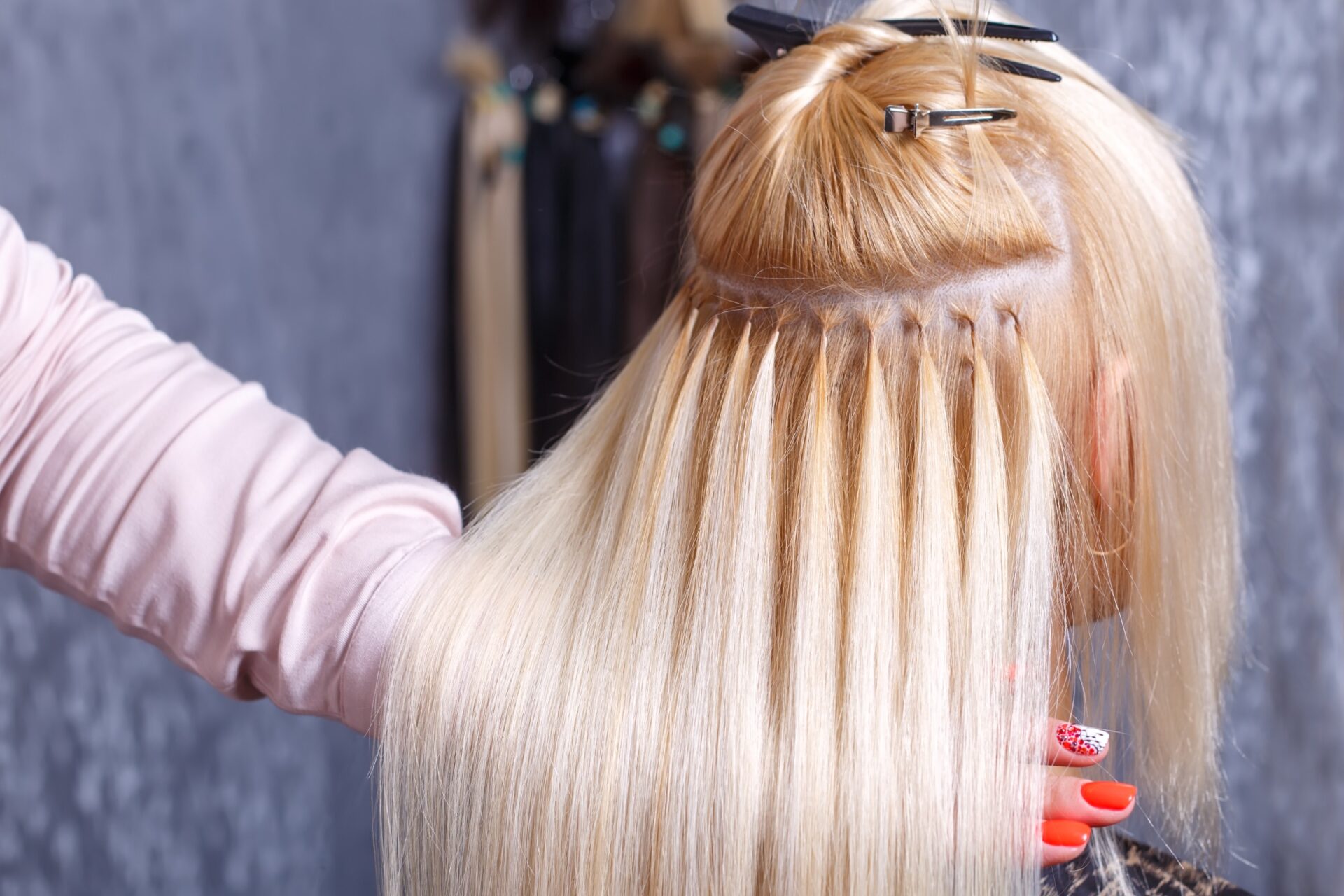 A stylist does hair extensions for a young girl with light hair.